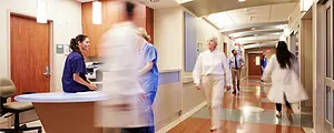 Doctors and nurses walk in a busy hospital hallway.