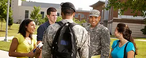 Two students in military uniforms talk with other students on a college campus.
