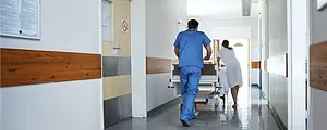 Two health care workers transport a patient through a hospital hallway on gurney