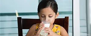A young girl drinks a glass of skim milk