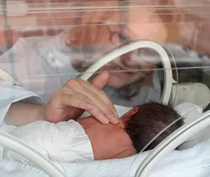 A woman touches a premature baby in an incubator