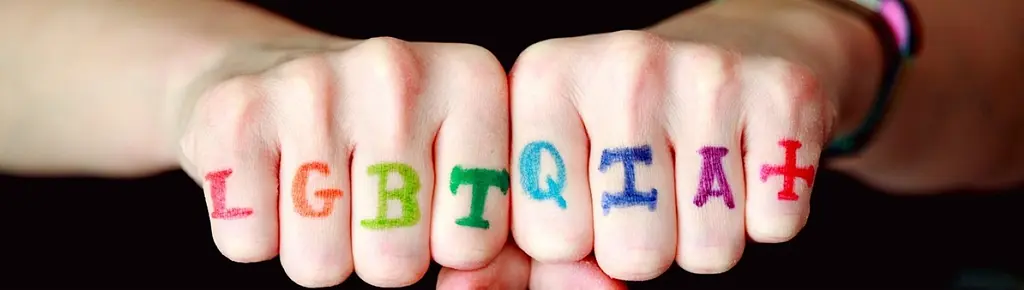 Photo of two fists next to each other, with one letter of LGBTQIA+ on each finger