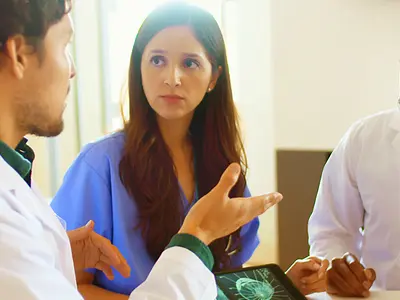 Two male doctors and a female doctor hold a discussion at a conference table.