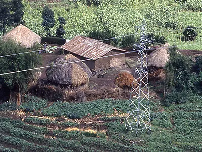 Power lines stretch over a traditional village in a wooded area of Rwanda.