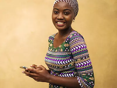 A young African woman reads text messages on a mobile phone.