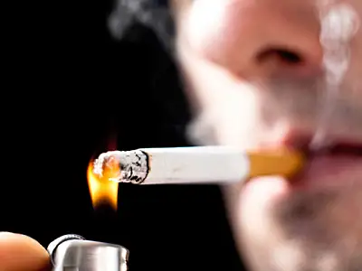 Cigarette being lit by a lighter, close-up view of a person's face in background.