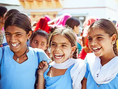 Three girls in India wearing matching light blue outfits and smiling for the camera.