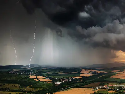 Lightning strikes amid ominous storm clouds above a rural landscape.