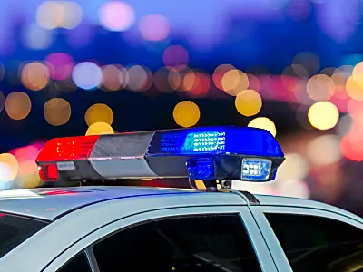 Red and blue lights from a police car flash against the background of a city skyline.