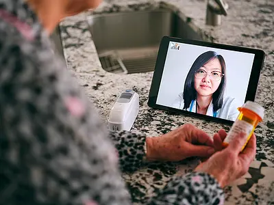 A senior woman meets with her doctor via a teleconferencing app on her phone.