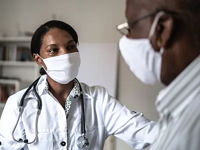 A Black female doctor works with a Black male patient. Both are wearing masks.