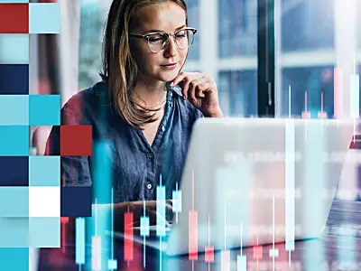 A woman works on a laptop amidst financial charts in a modern, bright office.