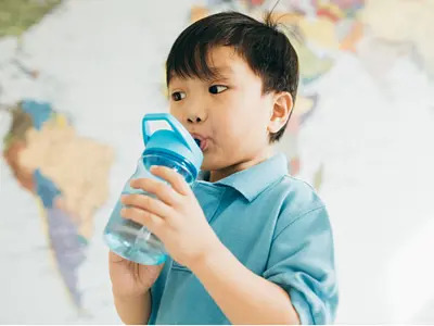 A young Asian child drinking from a water bottle in front of a map