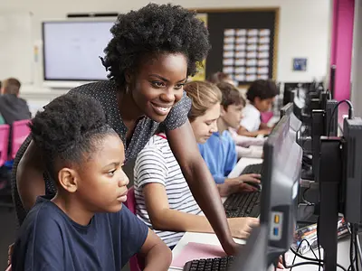 Teacher Helping Female Pupil Line Of High School Students Working at Screens In Computer Class