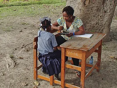 Child at desk outside with teacher