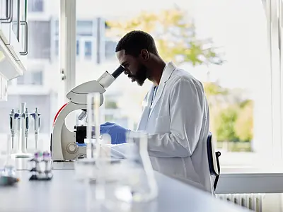 Photo of a Black scientist in a lab looking into a microscope