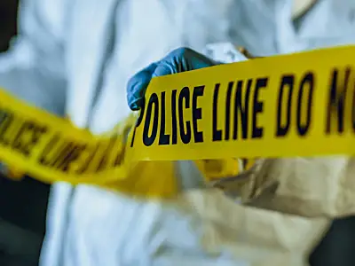 Photo of a forensic investigator unrolling police tape to mark off a crime scene