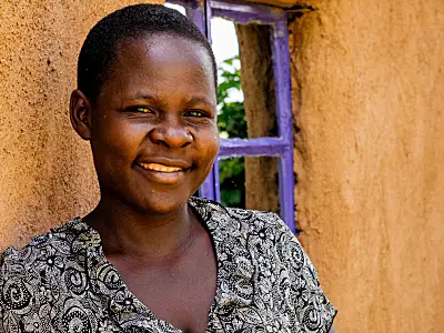 A smiling Kenyan woman standing outside a house.