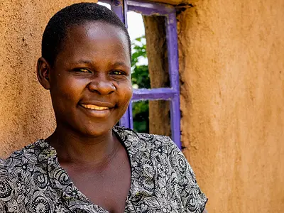A smiling Kenyan woman standing outside a house.