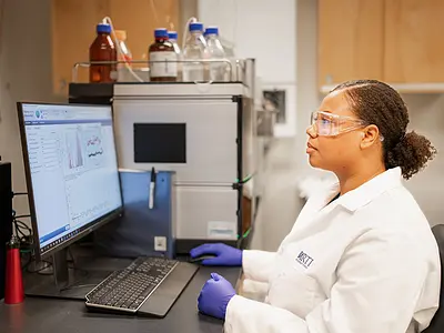 Imari Walker-Franklin wearing a lab coat sitting at a computer with data on the screen