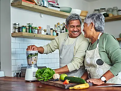 Photo of an elderly couple smiling in their kitchen while cooking a healthy meal