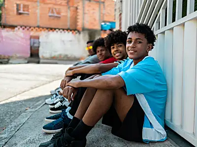 Photo of teenage boys of color smiling while sitting on the street