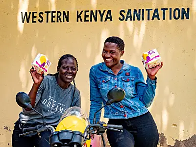 Photo of two Kenyan women smiling holding sanitary products near a motorbike