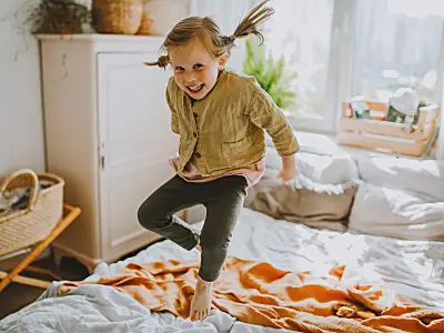 Photo of a girl smiling and jumping on a bed