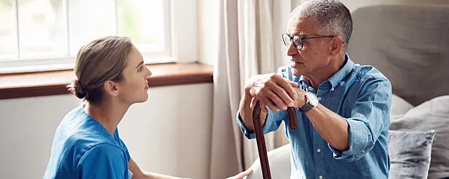 A female health care worker visits a senior male patient at his home.