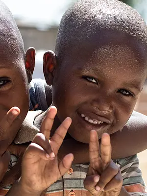 Two Haitian children hug and smile in a courtyard.
