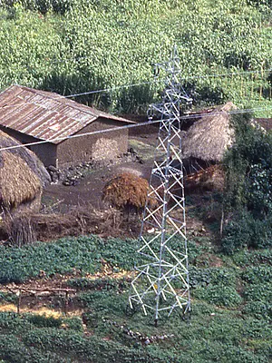Power lines stretch over a traditional village in a wooded area of Rwanda.