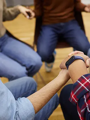 A closeup of a circle of people holding hands, as if participating in a support group.