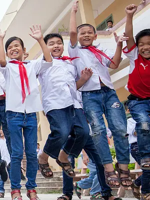 Schoolchildren in Vietnam hold hands, smile, and jump.