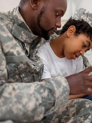 Photo of a father in miltary uniform looking at a phone with his tween son