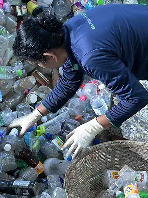 A woman collects bottles from a heap of plastic waste.