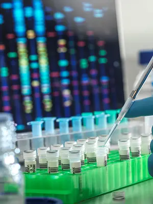 Close up photo of a scientist pipetting liquid into tubes in front of a colorful computer screen