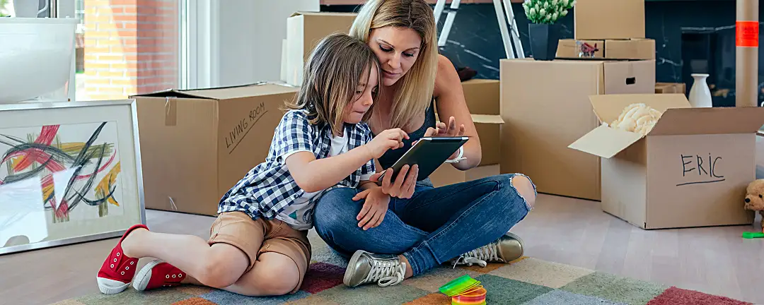 A mother and her son sit on the floor in their new home, surrounded by packed boxes.