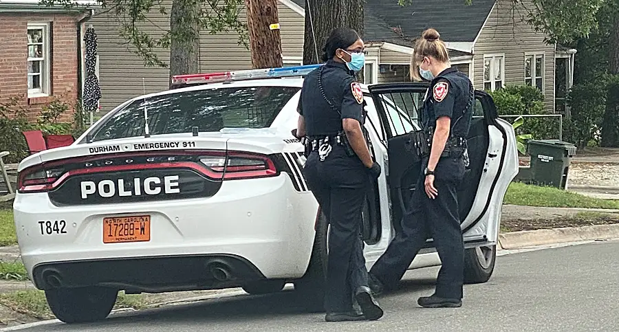 Two female Durham Police officers stand by a squad car. 