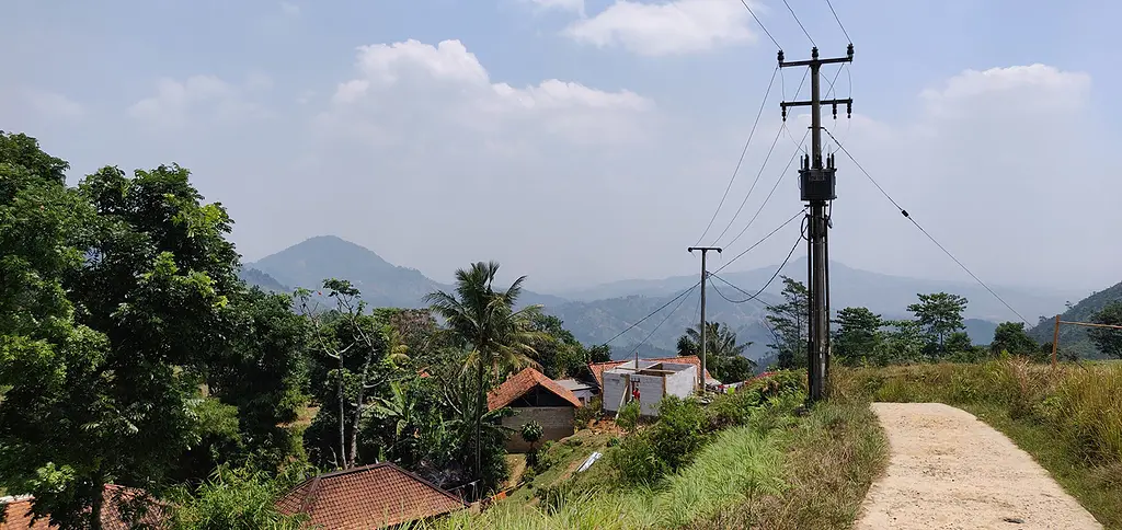 A power line runs along a dirt road in Indonesia.