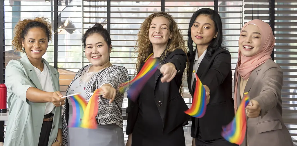 Group of coworkers waving Pride flags to celebrate LGBTQ+ inclusivity at work.
