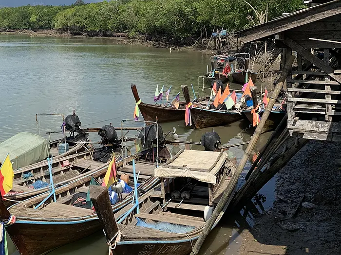 Fishing boats tied to a pier along a river in Southeast Asia.