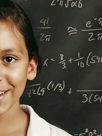 A young student in front of a chalkboard with equations written on it