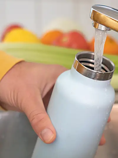 Hand holding water bottle under water faucet