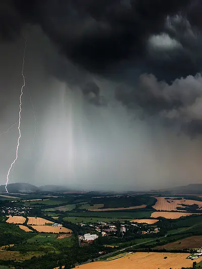 Lightning strikes amid ominous storm clouds above a rural landscape.