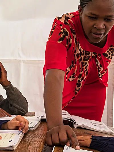 Teacher helping student with workbook. Two other students sitting beside