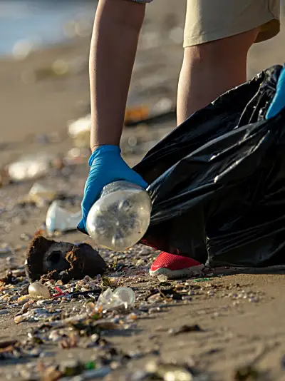 Person with gloves on picking up trash along the shoreline 