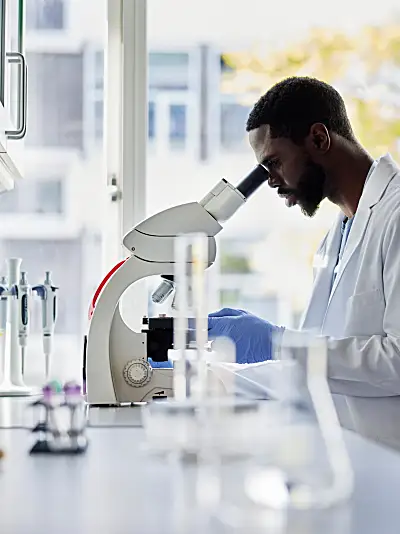 Photo of a Black scientist in a lab looking into a microscope