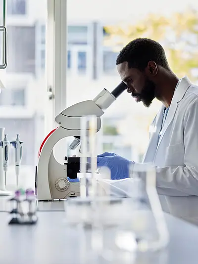 Photo of a Black scientist in a lab looking into a microscope