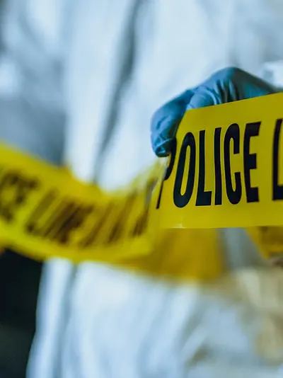 Photo of a forensic investigator unrolling police tape to mark off a crime scene