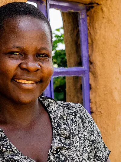 A smiling Kenyan woman standing outside a house.